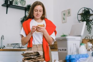 smiling woman sorting waste and using smartphone