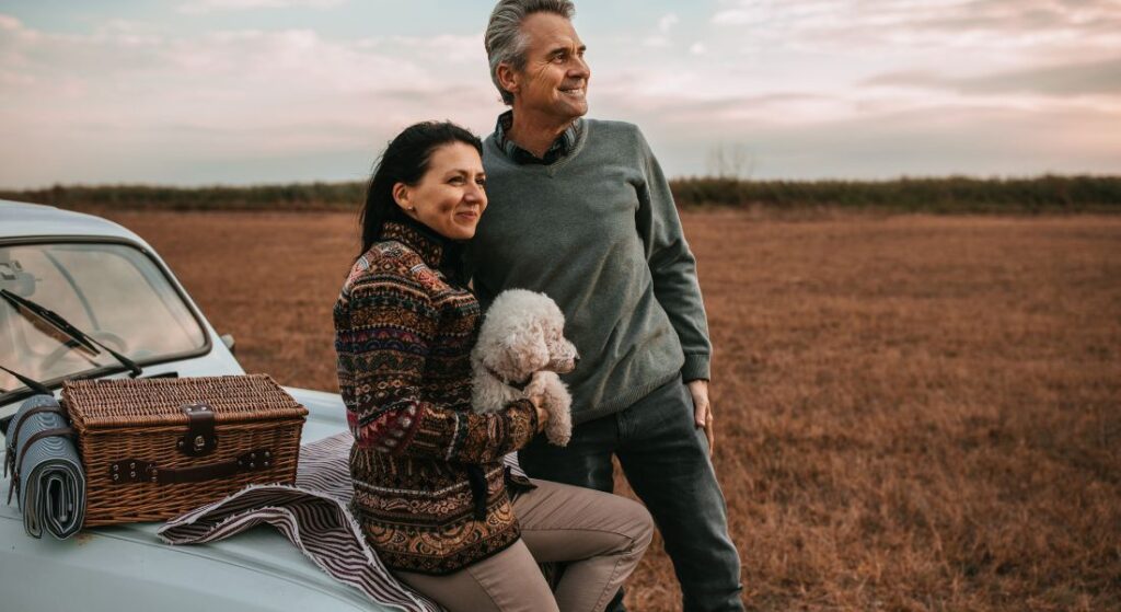 A couple sitting on the hood of a car in a field.